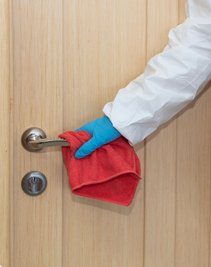 Close-up image of a cleaner disinfecting the doorknobs with red microfiber.